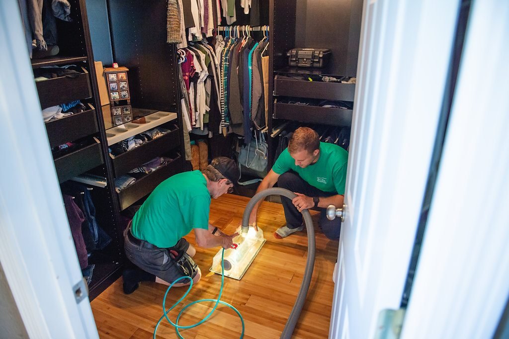Two Smart Centreville technicians in green shirts cleaning air ducts inside a Centreville home