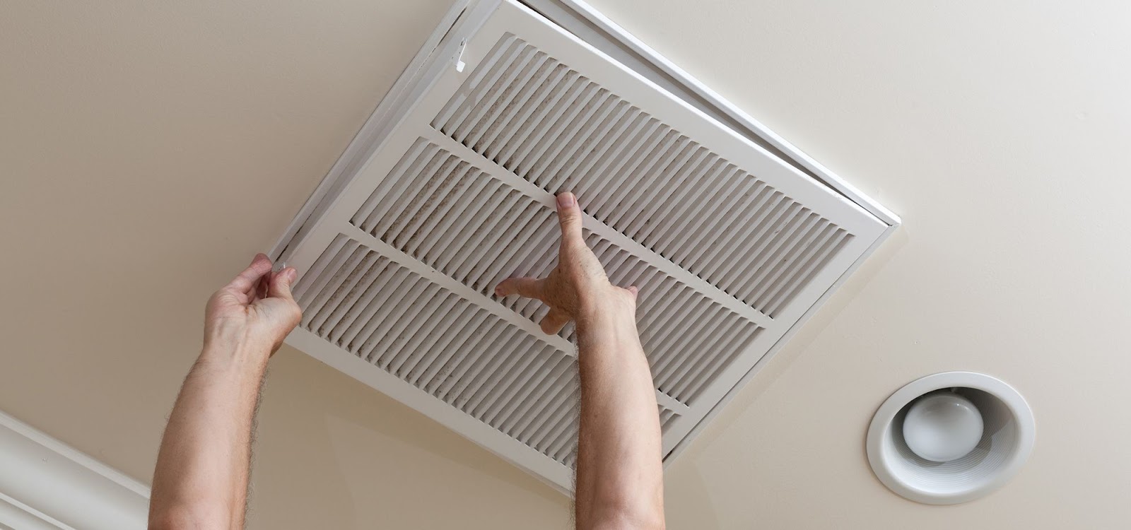 Technician removing a ceiling return-air vent grille to clean the duct behind it